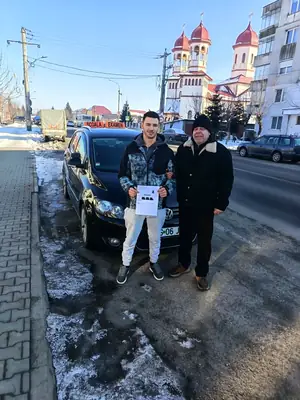 Cursant admis, cu foaia de examen în mână, lângă mașina școlii