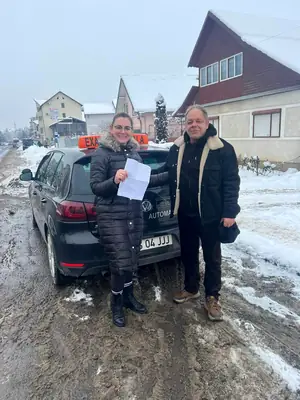 Cursant admis, cu foaia de examen în mână, lângă mașina școlii