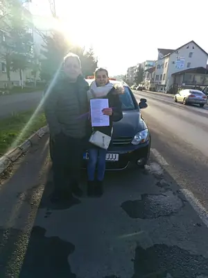 Cursant admis, cu foaia de examen în mână, lângă mașina școlii