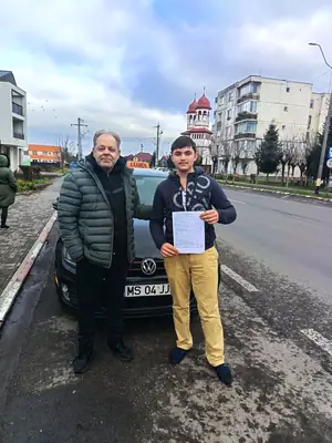 Cursant admis, cu foaia de examen în mână, lângă mașina școlii