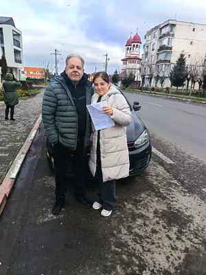 Cursant admis, cu foaia de examen în mână, lângă mașina școlii
