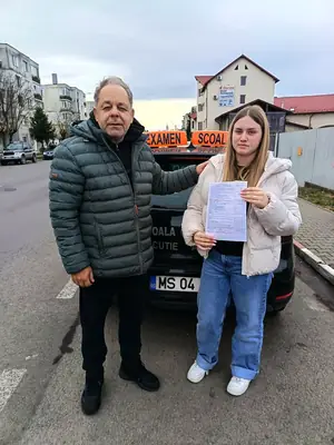 Cursant admis, cu foaia de examen în mână, lângă mașina școlii