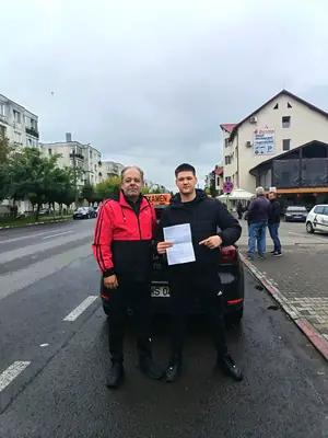 Cursant admis, cu foaia de examen în mână, lângă mașina școlii