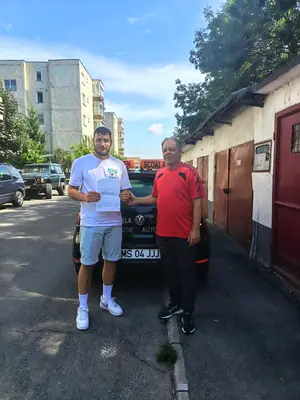 Cursant admis, cu foaia de examen în mână, lângă mașina școlii
