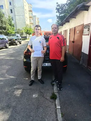 Cursant admis, cu foaia de examen în mână, lângă mașina școlii