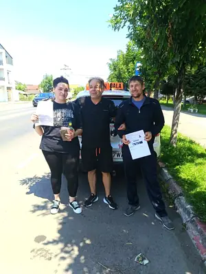 Cursant admis, cu foaia de examen în mână, lângă mașina școlii