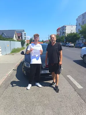 Cursant admis, cu foaia de examen în mână, lângă mașina școlii