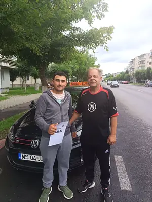 Cursant admis, cu foaia de examen în mână, lângă mașina școlii