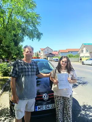 Cursant admis, cu foaia de examen în mână, lângă mașina școlii