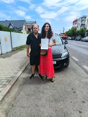 Cursant admis, cu foaia de examen în mână, lângă mașina școlii