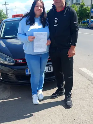 Cursant admis, cu foaia de examen în mână, lângă mașina școlii