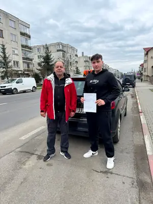 Cursant admis, cu foaia de examen în mână, lângă mașina școlii