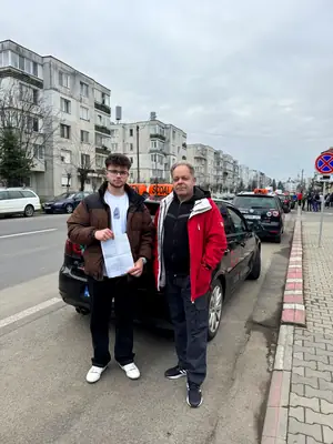 Cursant admis, cu foaia de examen în mână, lângă mașina școlii