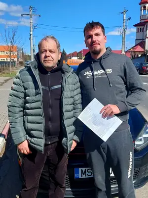 Cursant admis, cu foaia de examen în mână, lângă mașina școlii