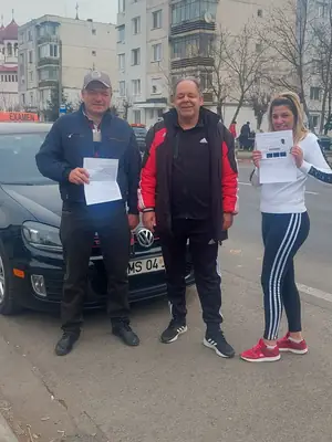 Cursant admis, cu foaia de examen în mână, lângă mașina școlii