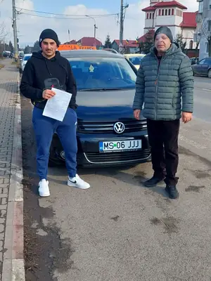 Cursant admis, cu foaia de examen în mână, lângă mașina școlii