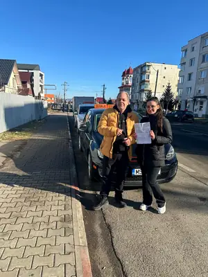 Cursant admis, cu foaia de examen în mână, lângă mașina școlii