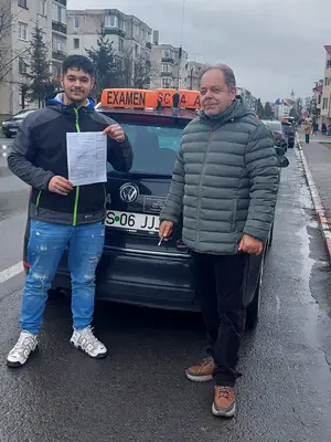 Cursant admis, cu foaia de examen în mână, lângă mașina școlii