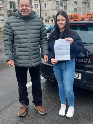 Cursant admis, cu foaia de examen în mână, lângă mașina școlii