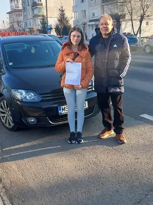 Cursant admis, cu foaia de examen în mână, lângă mașina școlii