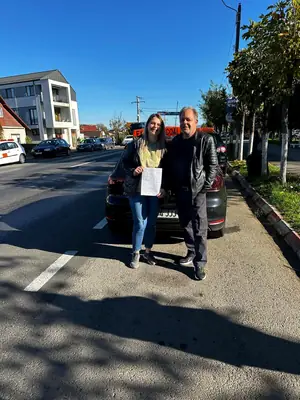 Cursant admis, cu foaia de examen în mână, lângă mașina școlii