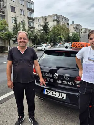 Cursant admis, cu foaia de examen în mână, lângă mașina școlii