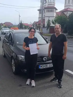 Cursant admis, cu foaia de examen în mână, lângă mașina școlii